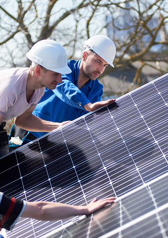 Zwei Arbeiter mit weißen Schutzhelmen montieren und überprüfen an einem sonnigen Tag im Freien Solarmodule und setzen dabei ihr Fachwissen im Bereich der Elektro- und Informationstechnik ein. Der eine trägt eine blaue Jacke, der andere ein helles Hemd. Im Hintergrund sind Bäume und Gebäude zu sehen. Zwei Arbeiter mit weißen Schutzhelmen montieren und überprüfen an einem sonnigen Tag im Freien Solarmodule und setzen dabei ihr Fachwissen im Bereich der Elektro- und Informationstechnik ein. Der eine trägt eine blaue Jacke, der andere ein helles Hemd. Im Hintergrund sind Bäume und Gebäude zu sehen.